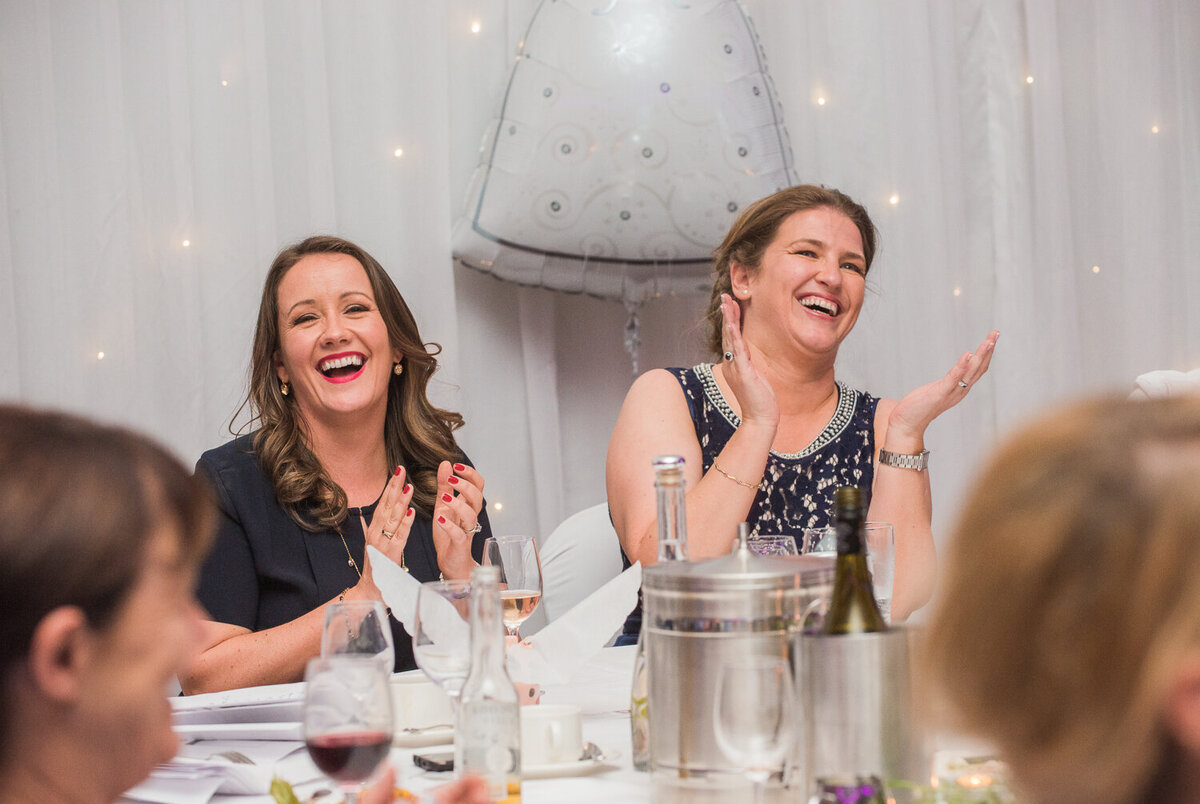 gay brides laughing and clapping at wedding reception