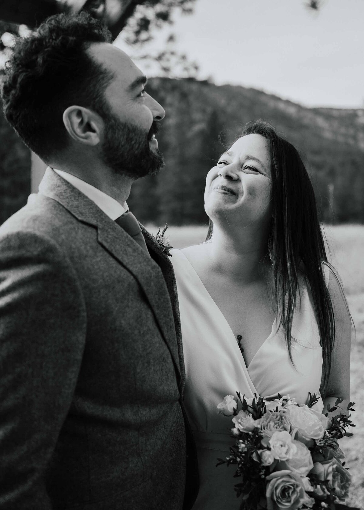 Maddie Rae Photography black and white of bride and groom standing next to each other. she is looking up at him and he is looking off into the distance past her. taken from the side of the groom. mountains in the background
