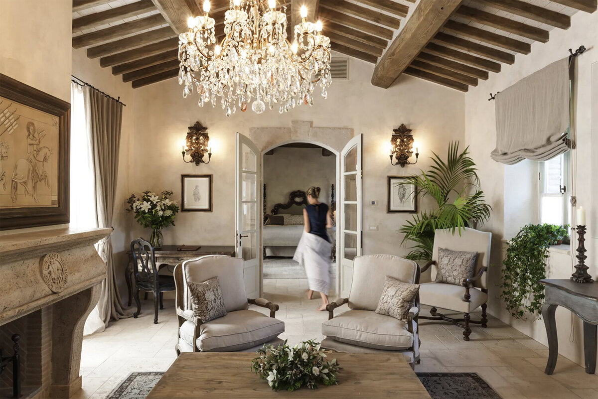 A refined, rustic Tuscan country living room at Borgo Sant Pietro with linen upholstered furniture, wooden sideboards, a stone fireplace and a crystal chandelier