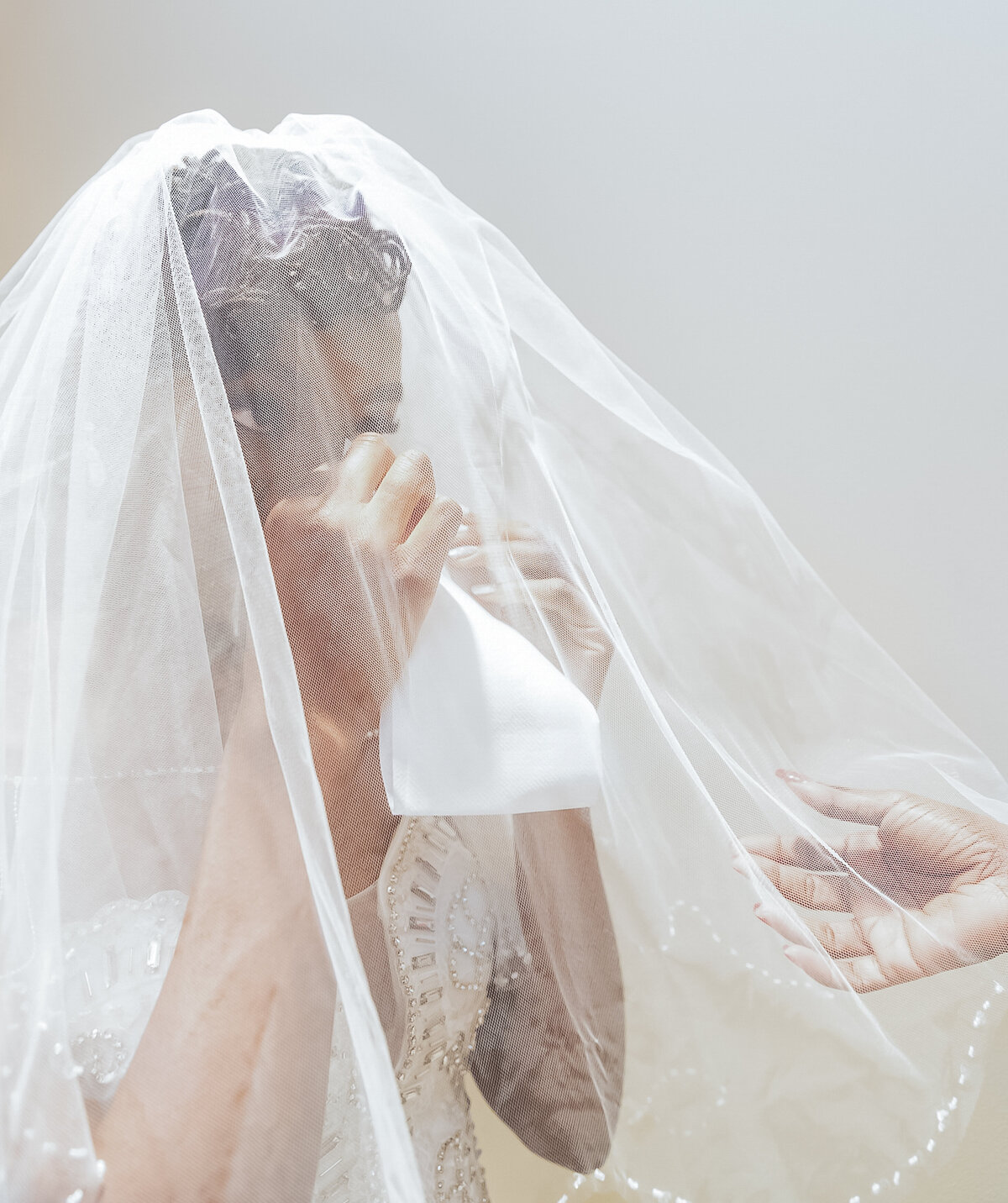 In the bridal suite on her wedding day, the bride is crying while wearing her veil.  The bridal suite has cream walls.