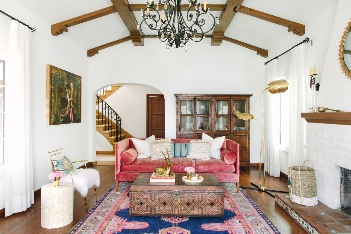 Colorful Spanish Revival living room with pink velvet sofa, Moroccan wood coffee table, Global Views Rimini floor lamp , and Caitlin Wilson Kismet rug