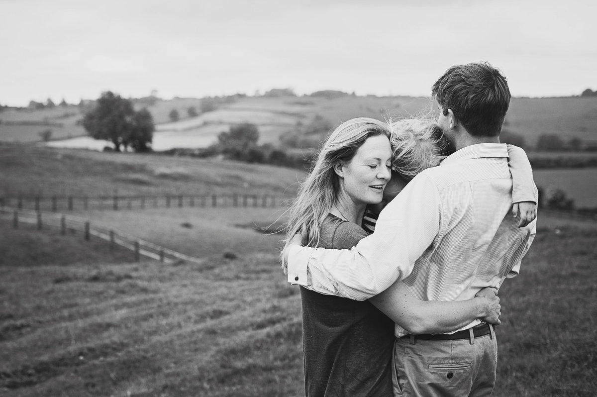 A father embraces his wife and children in a field during a family photo shoot