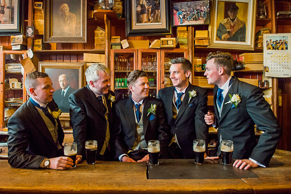 Groom and groomsmen sitting in traditional Irish pub, wearing morning suits and drinking Guinness