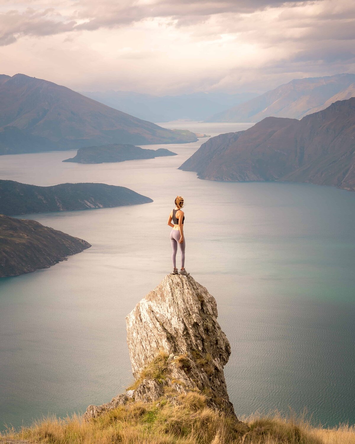 Woman standing on a rock looking at water and mountains below