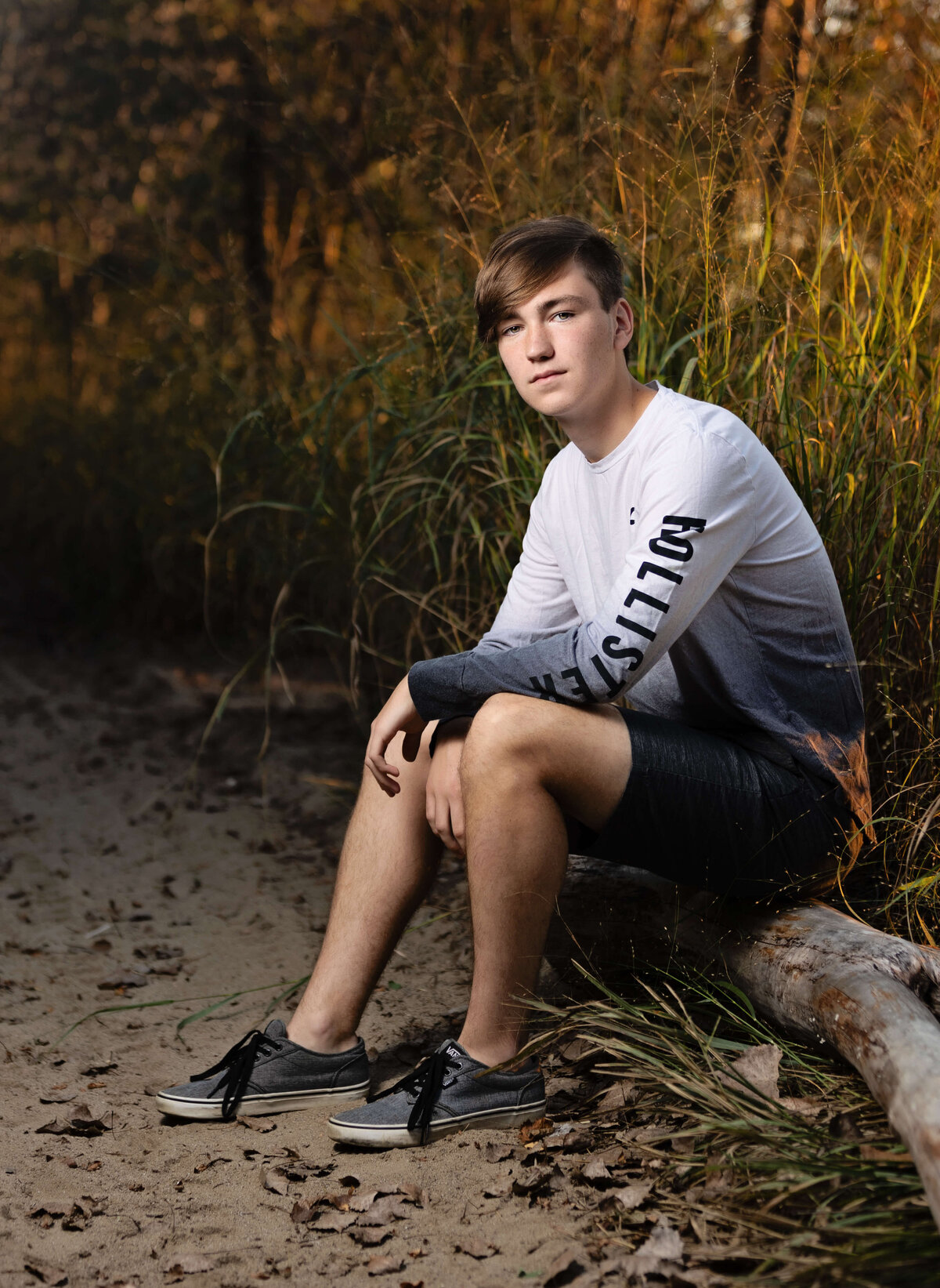 Photo of a high school senior boy sitting on a log at Presque Isle State Park in Erie Pa