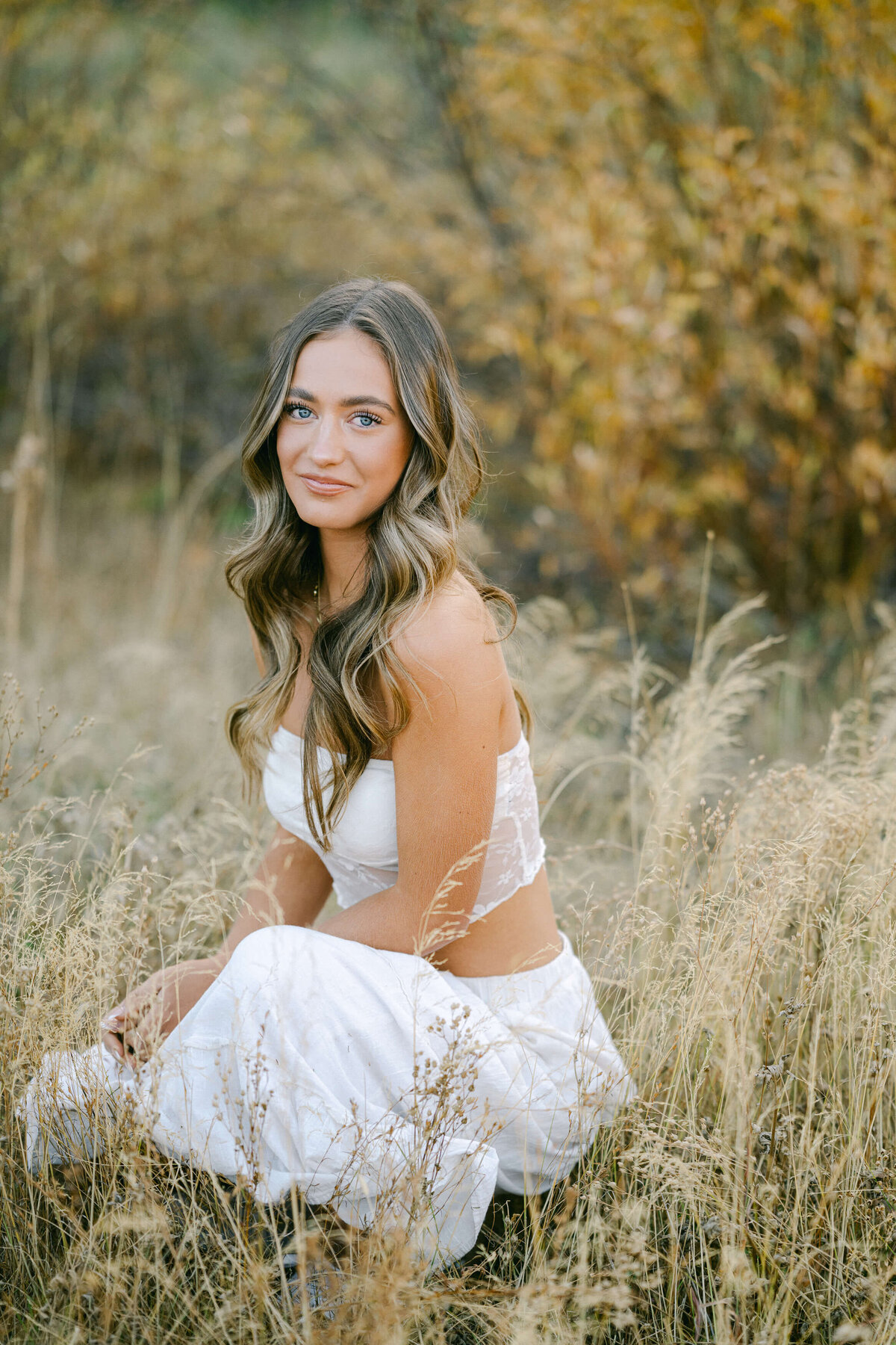 senior grad girl truckee high in white dress sitting in high weeds in meadow in tahoe