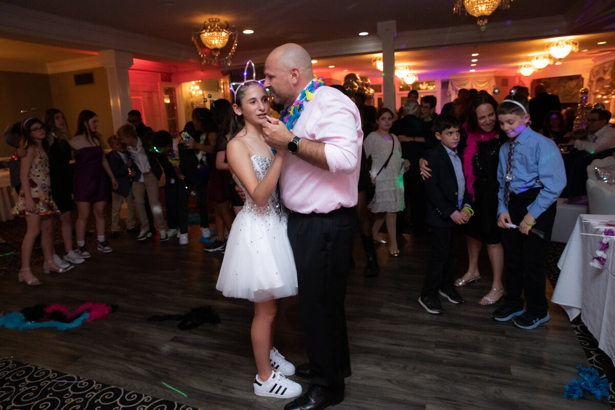 A teenage girl in a white dress dances with her father wearing a pink shirt at her bat mitzvah Portobello's Oakland New Jersey bat mitzvah Bergen County bar photographer Milestone Images
