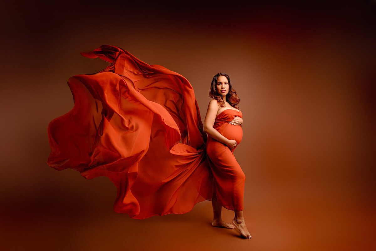 mother is wrapped in a rust chiffon with the fabric flowing behind her while standing on a brown background