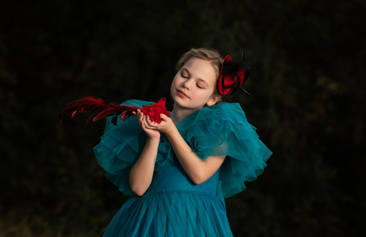 girl-in-blue-dress-and-red-hat-holding-red-bird