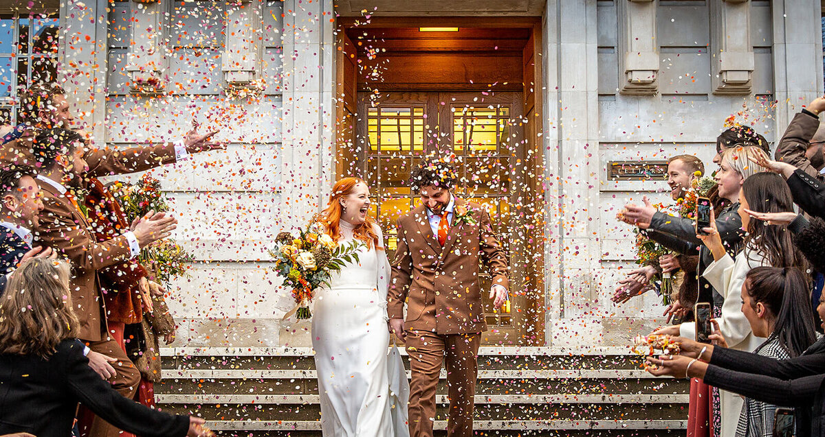 Bride and groom confetti exit Hackney Town Hall. Red head bride