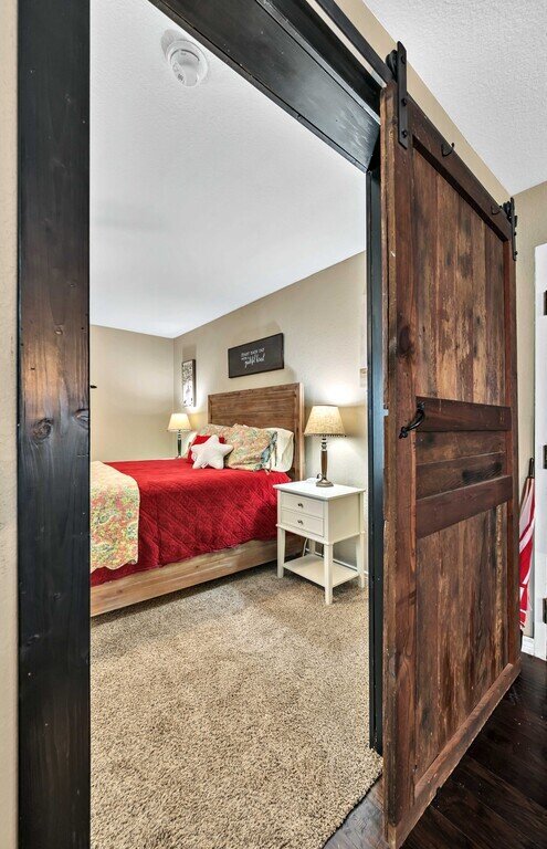 Bedroom with sliding barn door and comfortable bedding in this four-bedroom, four-bathroom vacation rental home and guest house with free WiFi, fully equipped kitchen, firepit and room for 10 in Waco, TX.