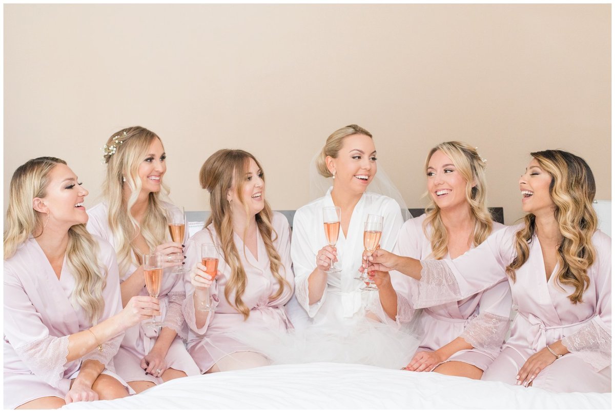 Light-and-Airy-Ottawa-Wedding-Photographer-bridesmaids-on-bed-champagne