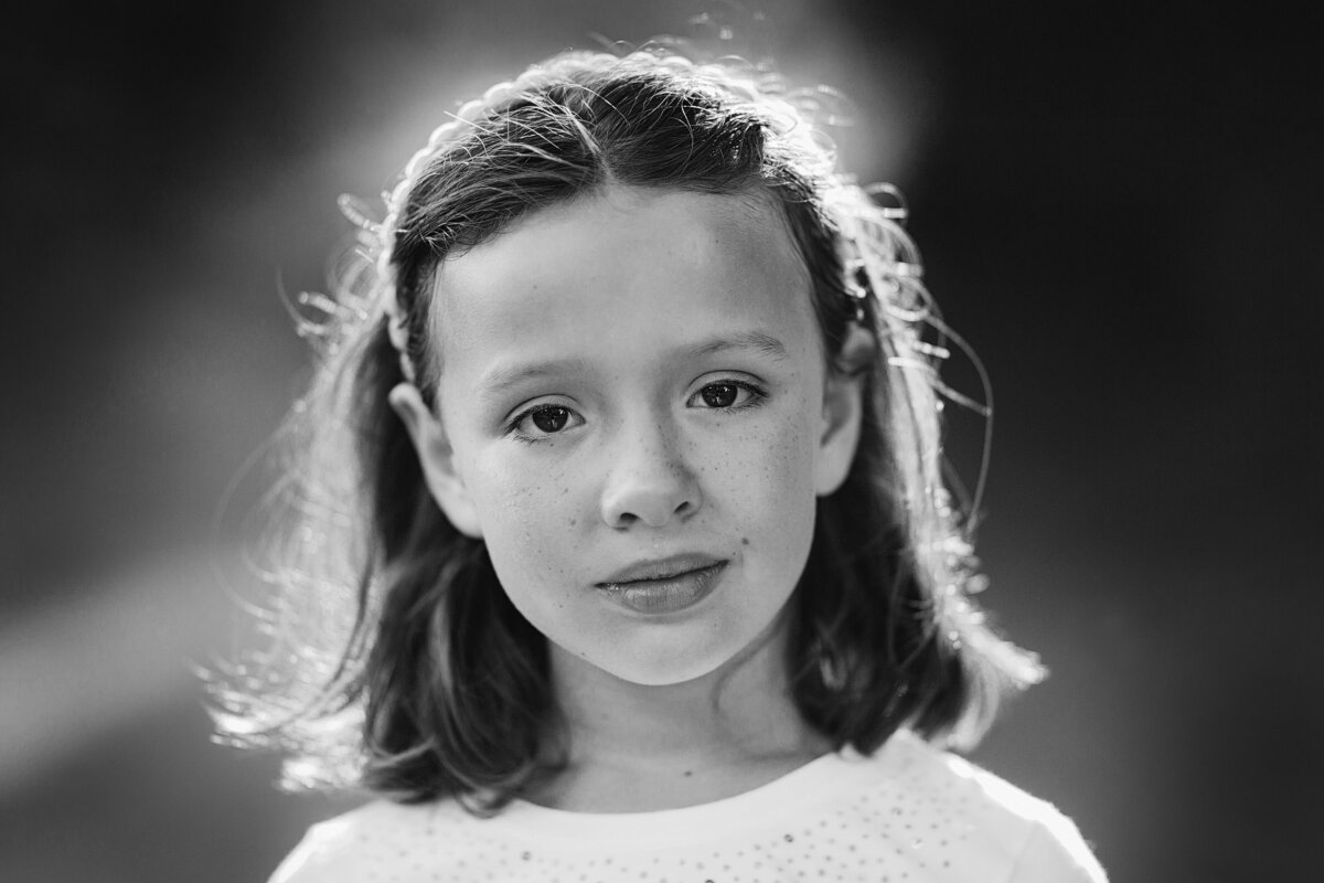 Black and white portrait of a girl at sunset with light coming behind her, she has big brown eyes.