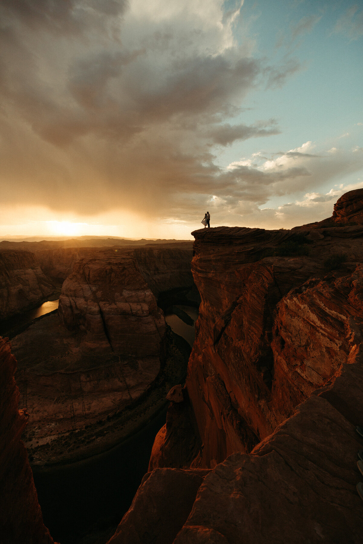 Wide angle shot of a silhouetted couple standing on a cliff at Horseshoe Bend at sunset