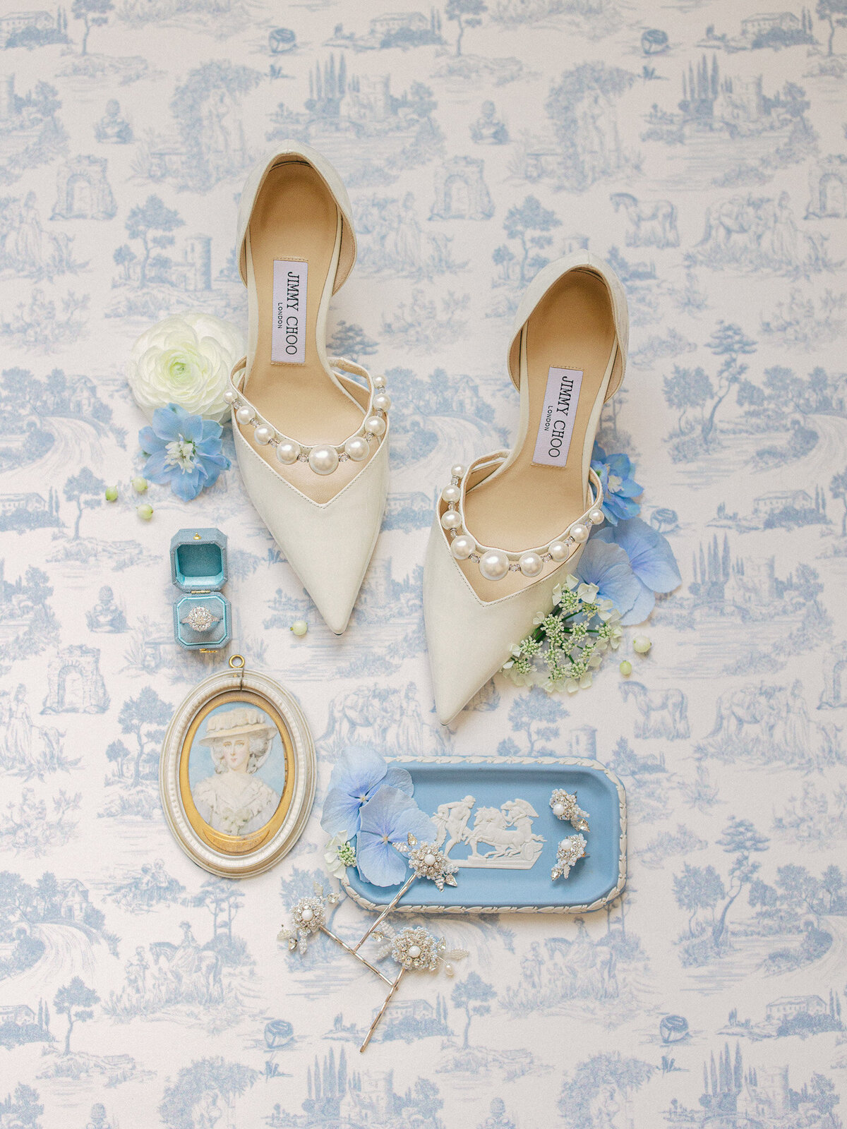Flat lay of wedding shoes, earrings, and ring on a blue and white toile background with blue and white flowers