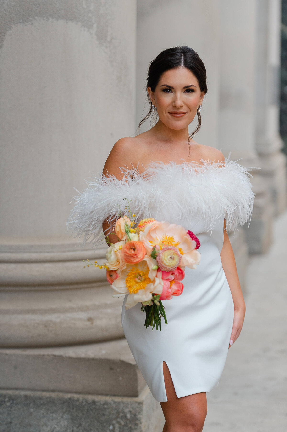 a bride in a short white dress with feathers holding an orange bouquet taken outside the NAC venue by Ottawa wedding photographer JEMMAN Photography