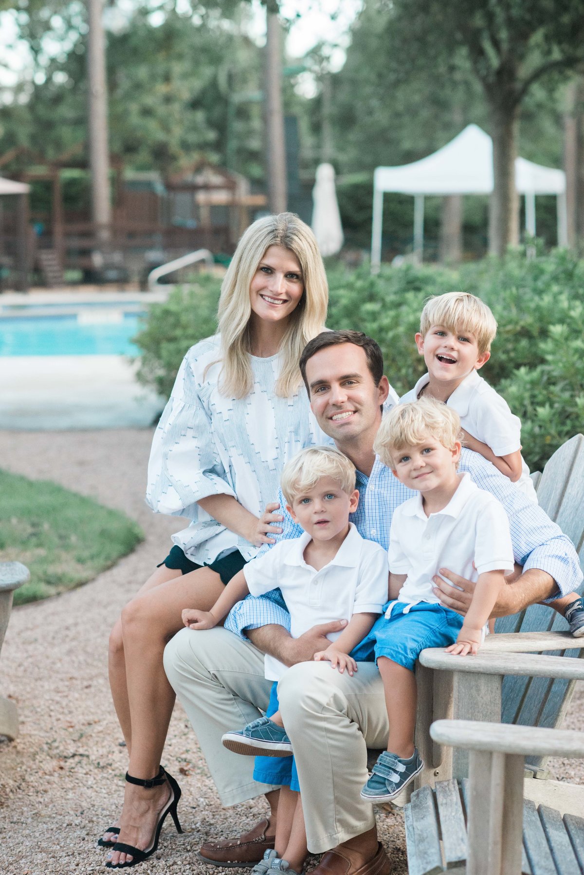 family of three young boys and parents in white and blue sitting on wooden chair at country club