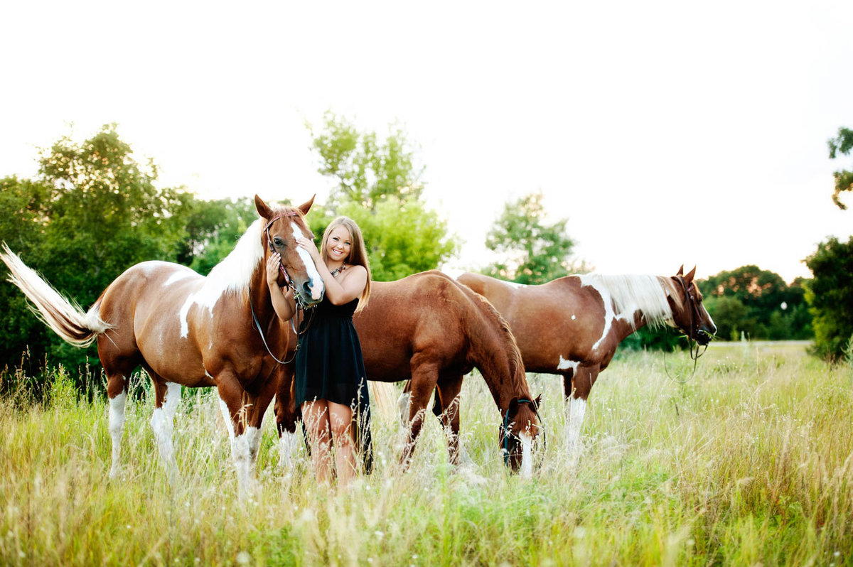 high school senior photo of girl in grass field with horses outfit idea