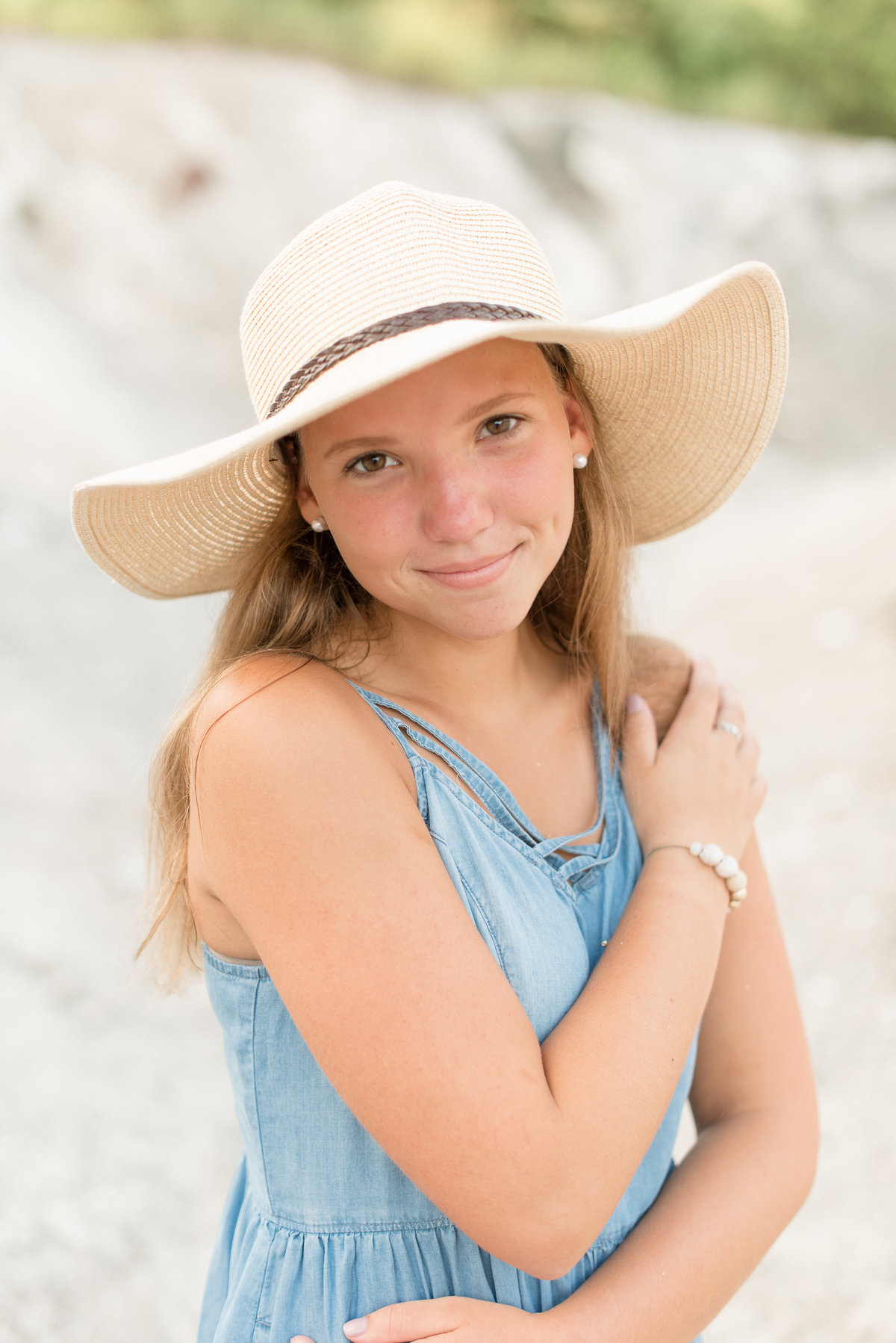 Senior girl barely smiling with right hand on left shoulder wearing fun summer hat in Lancaster, Pennsylvania.