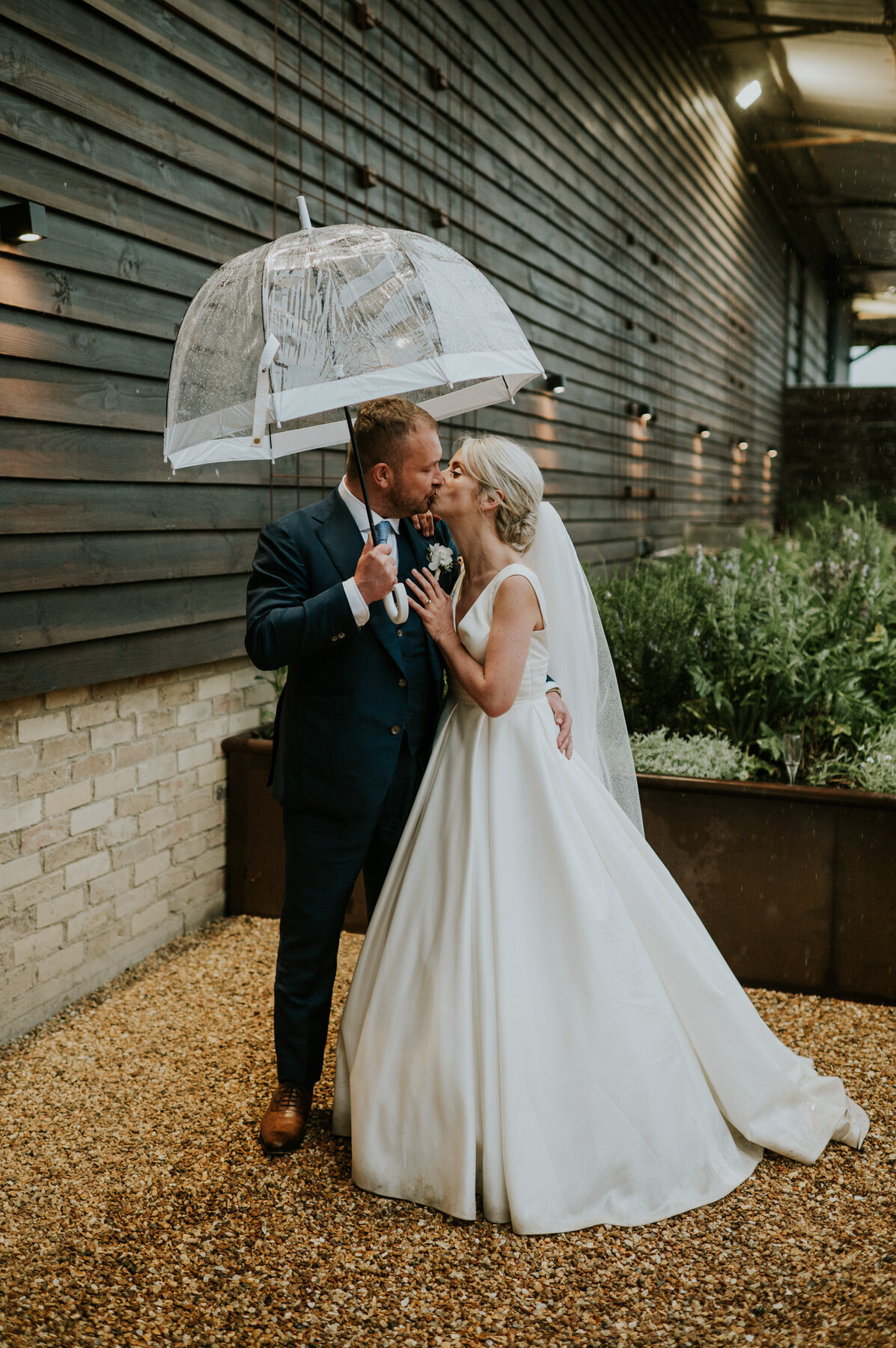 bride and groom kissing under umbrella in rain