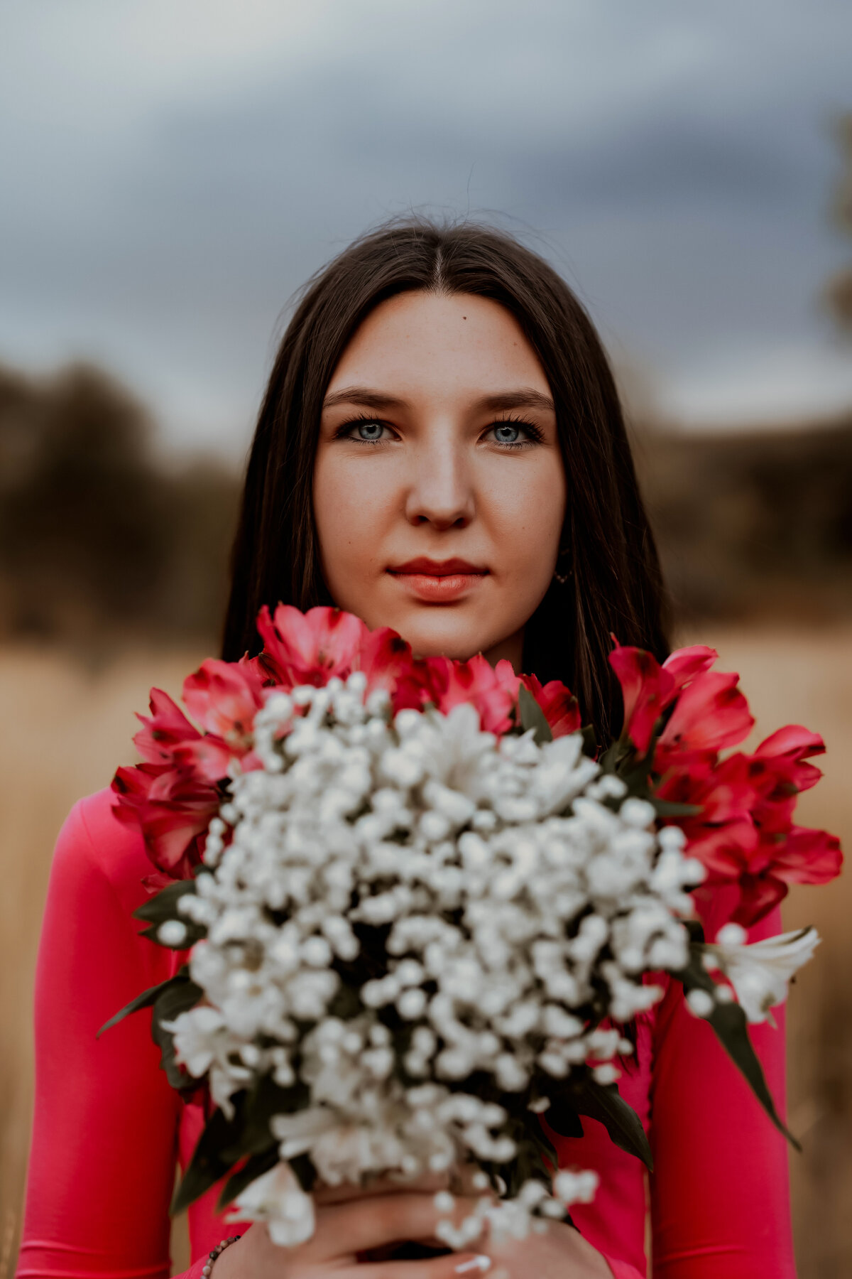 high school seniort girl holds hot pink flowers that match her shirt near her face for photos in boulder colorado