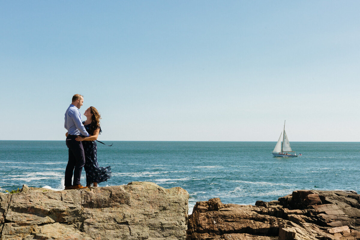 A couple holding each other as they stand on a rock overlooking the ocean.
