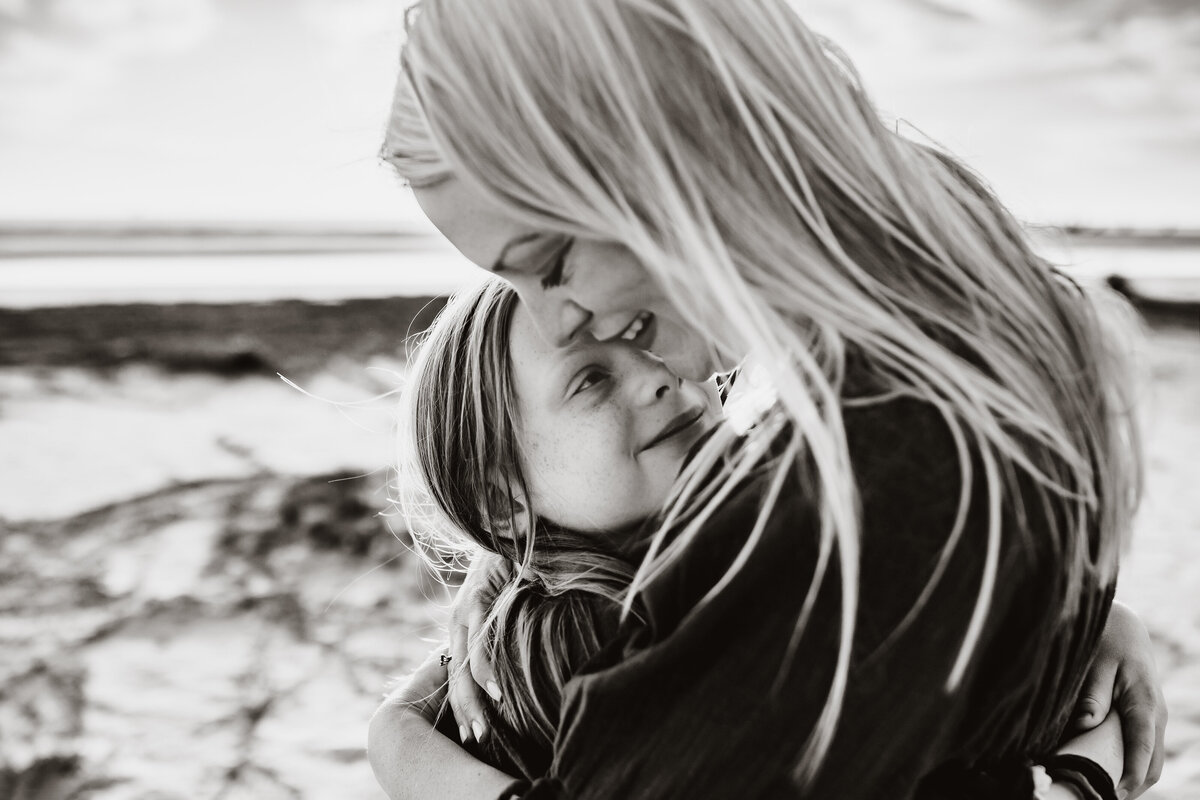 black and white beach portrait of a older child hugging her mom