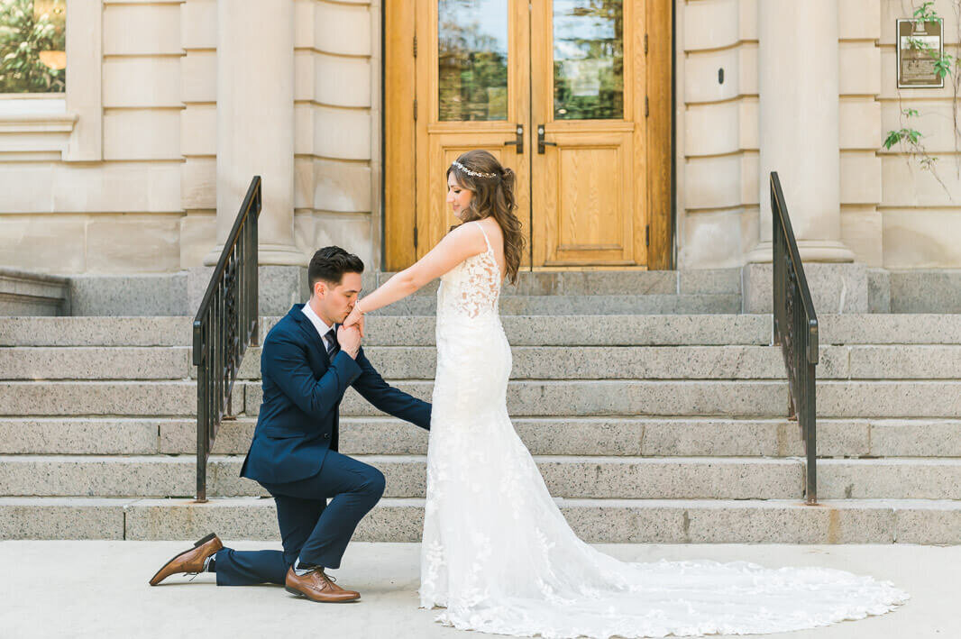 A groom kneels in front of his bride and kisses his hand at the University of Alberta in Edmonton, Alberta