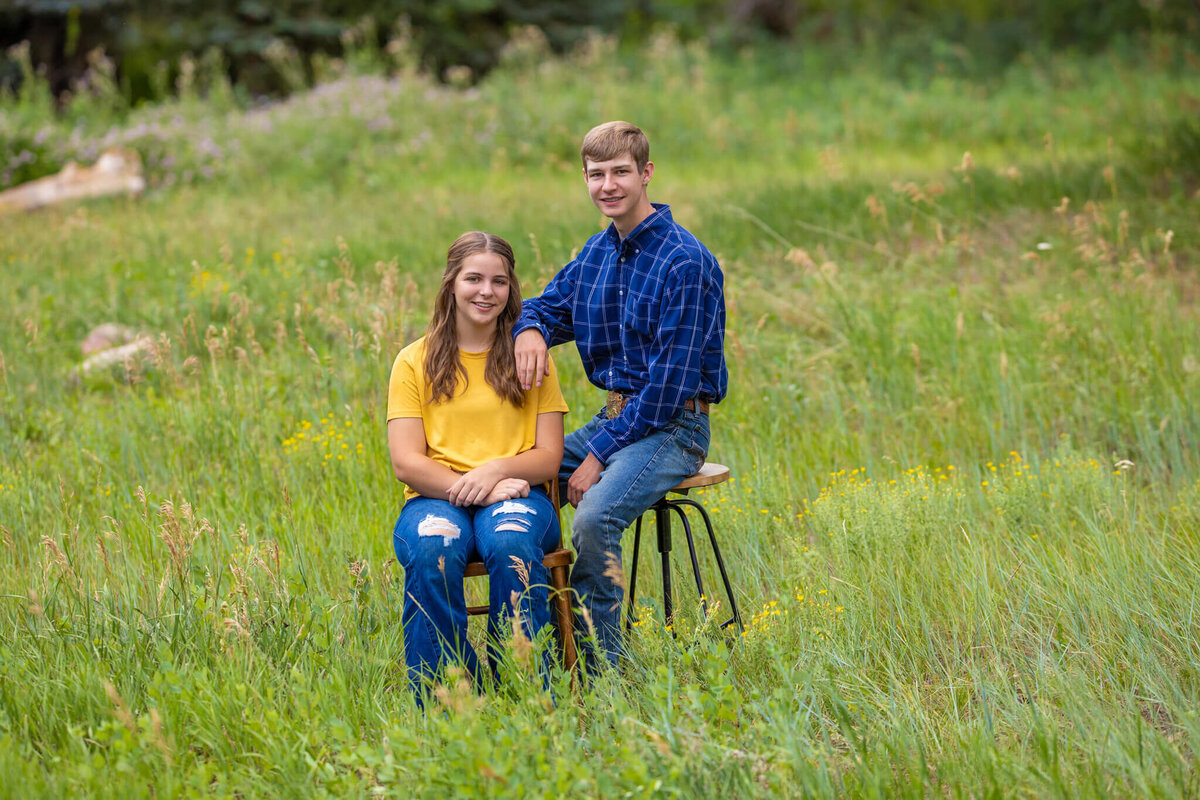 brother snd sister sitting on a chair and stool in a grassy field laughing