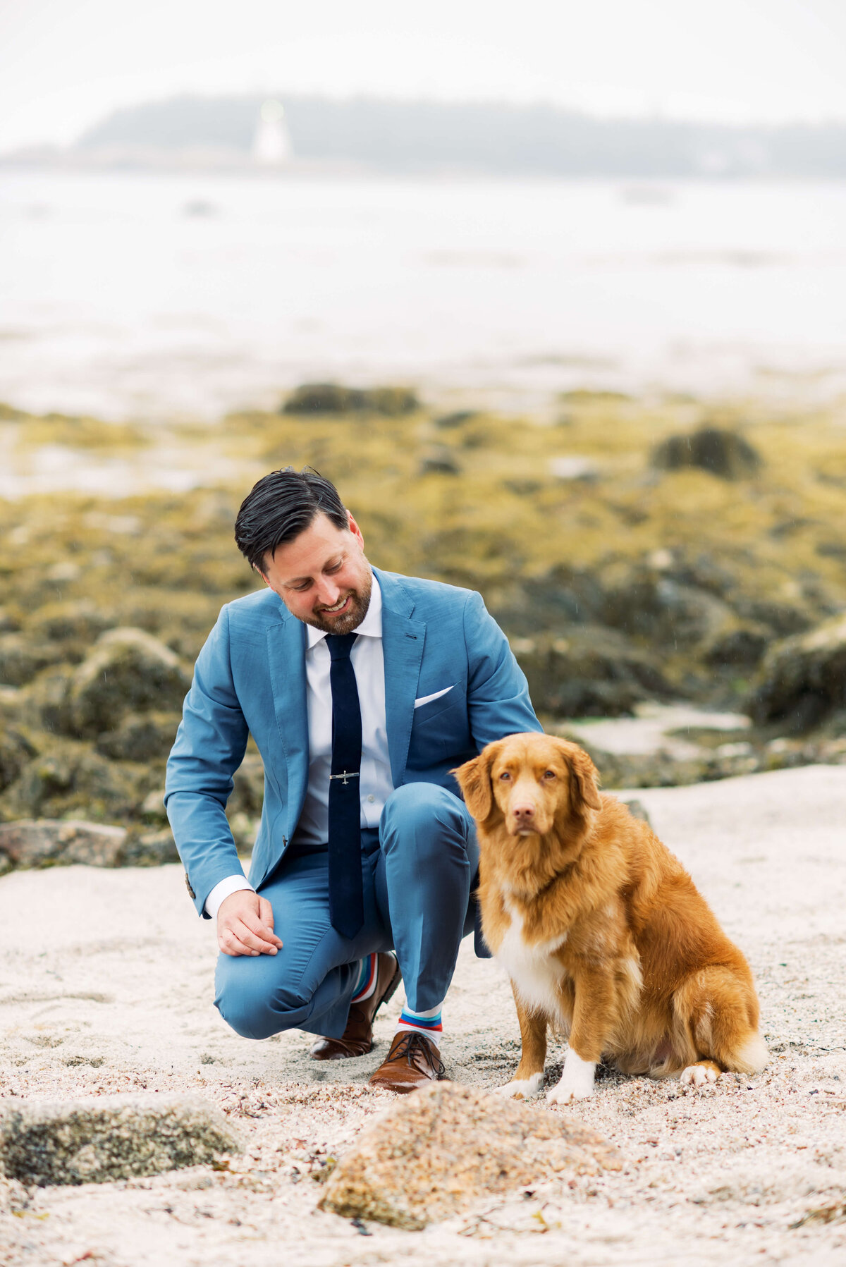Groom wearing blue suit with dog on beach at Oceanstone Resort Wedding in Nova Scotia