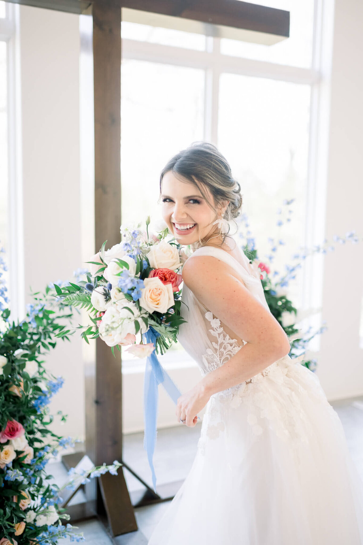 bride in white dress holds colorful bouquet and laughs towards camera