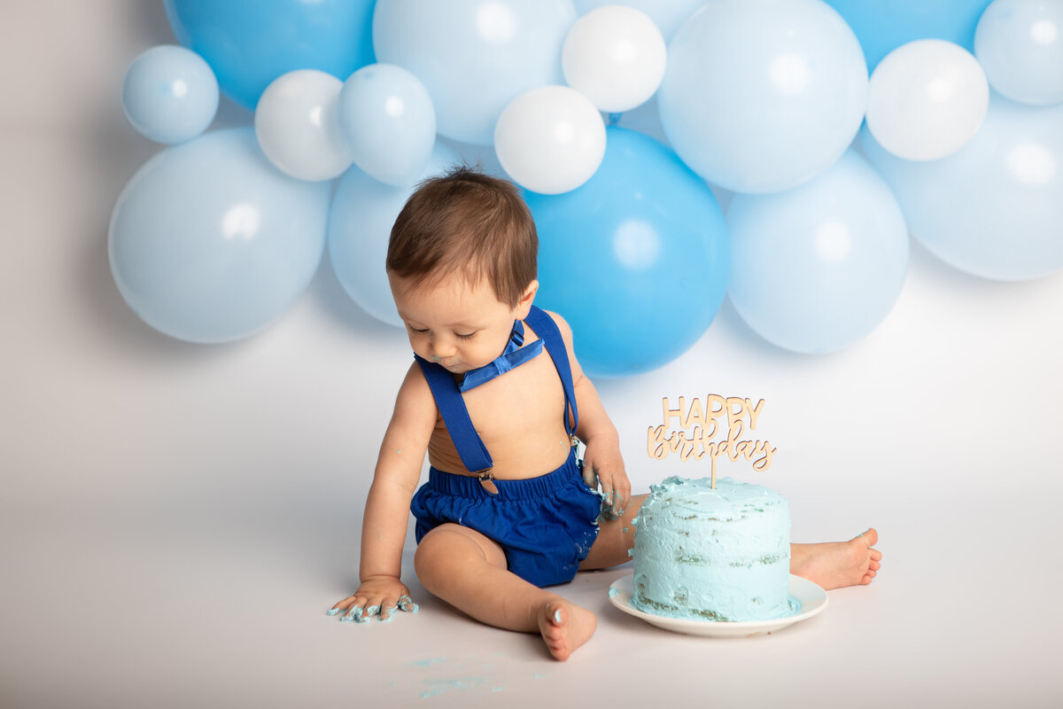 Birthday baby boy with a blue cake and balloons