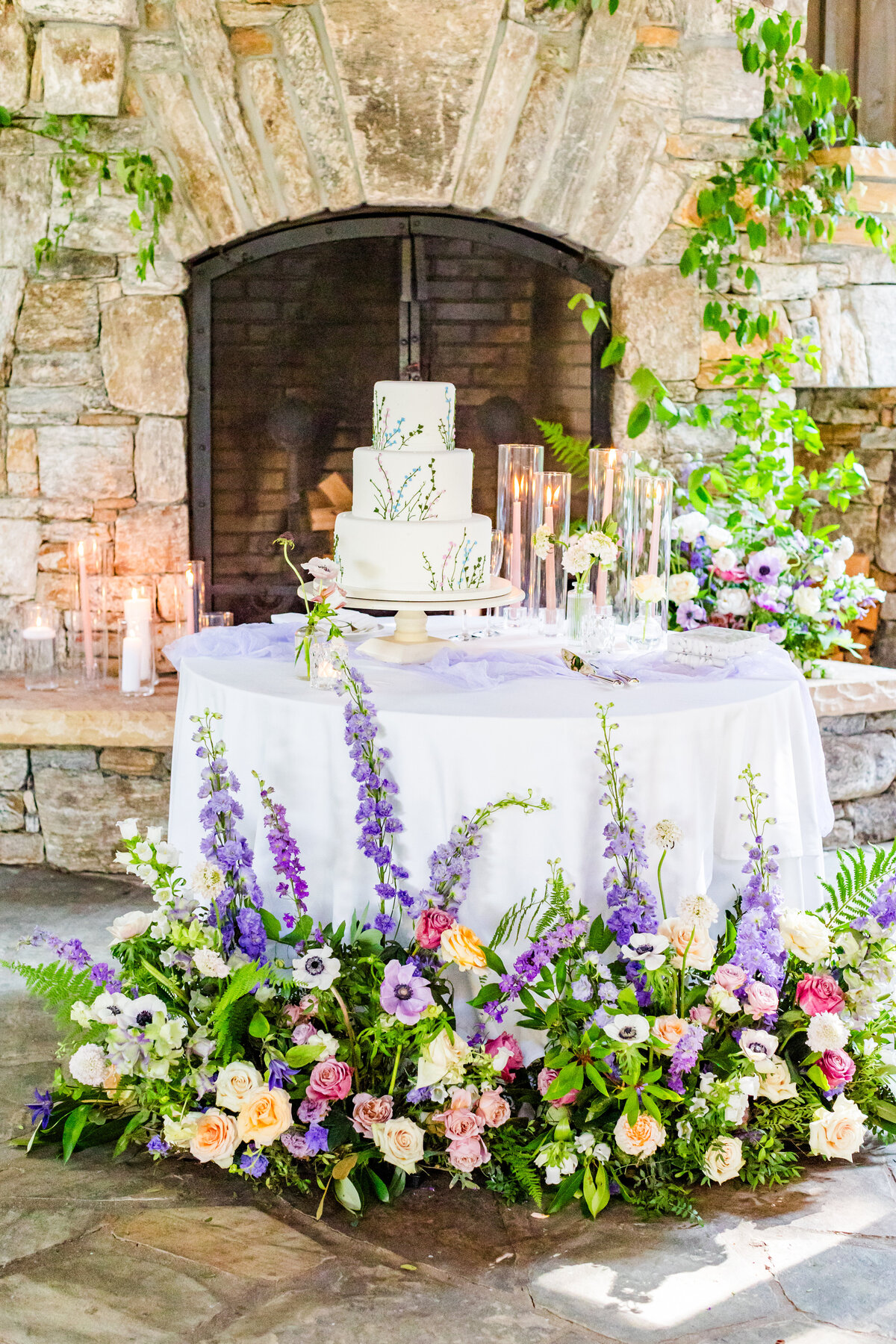 shades of spring purple florals around cake table in front of fireplacewedding table settings at the Farm at Old Edwards in North Carolina
