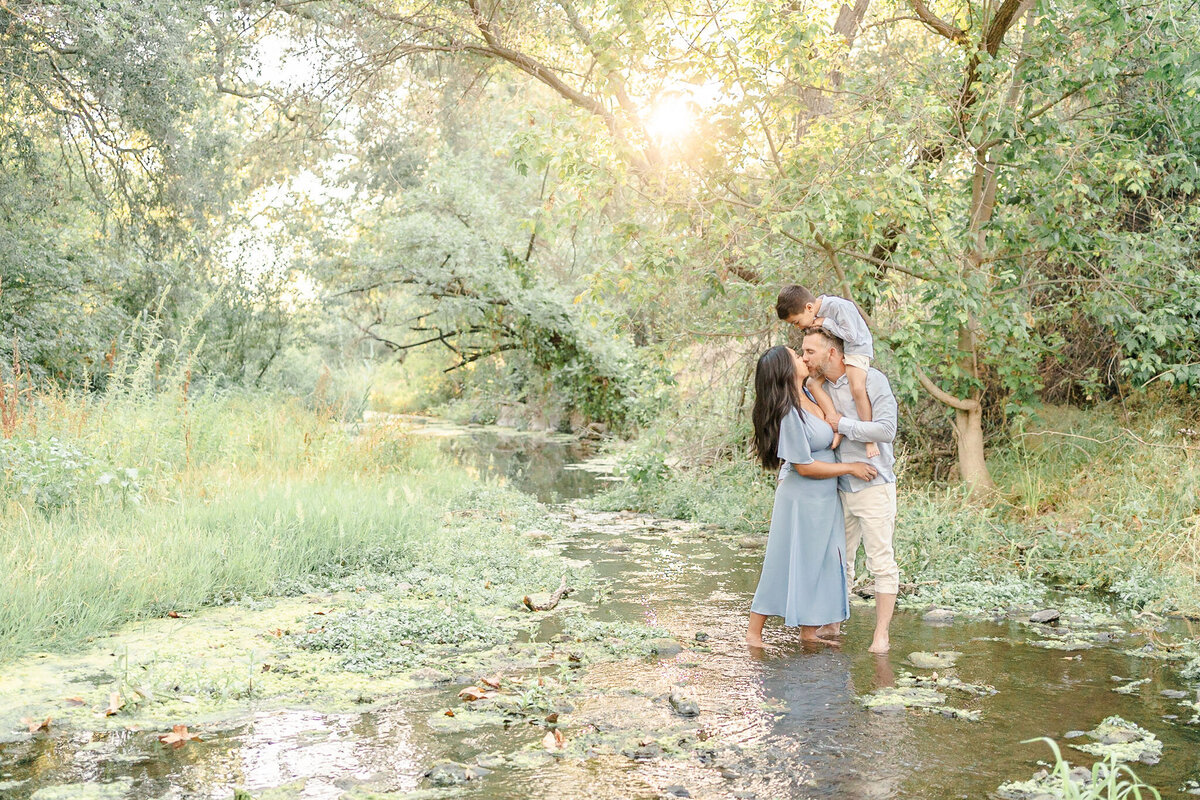 bay area family standing in a creek with the son on dad's shoulders while mom and dad kiss