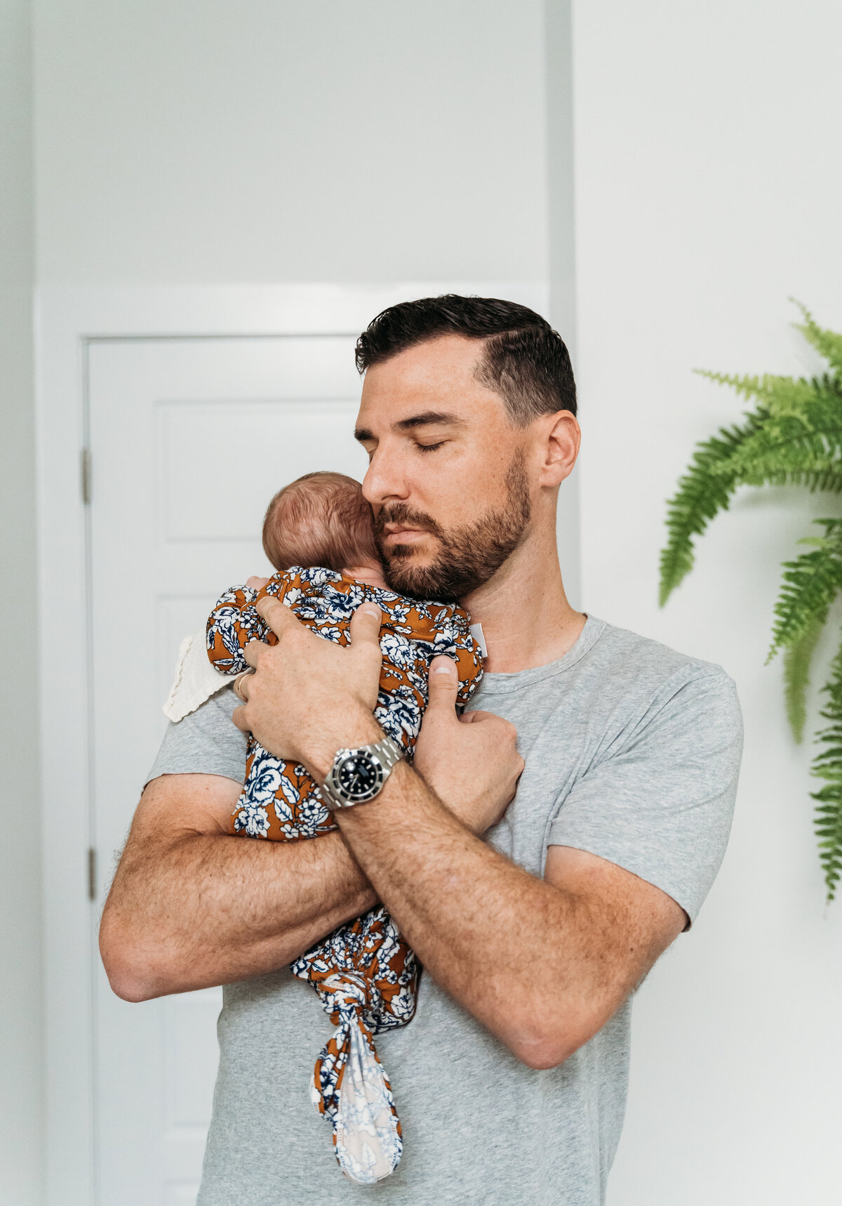 Newborn Photographer, a dad stands holding baby in his home, taking in the moment