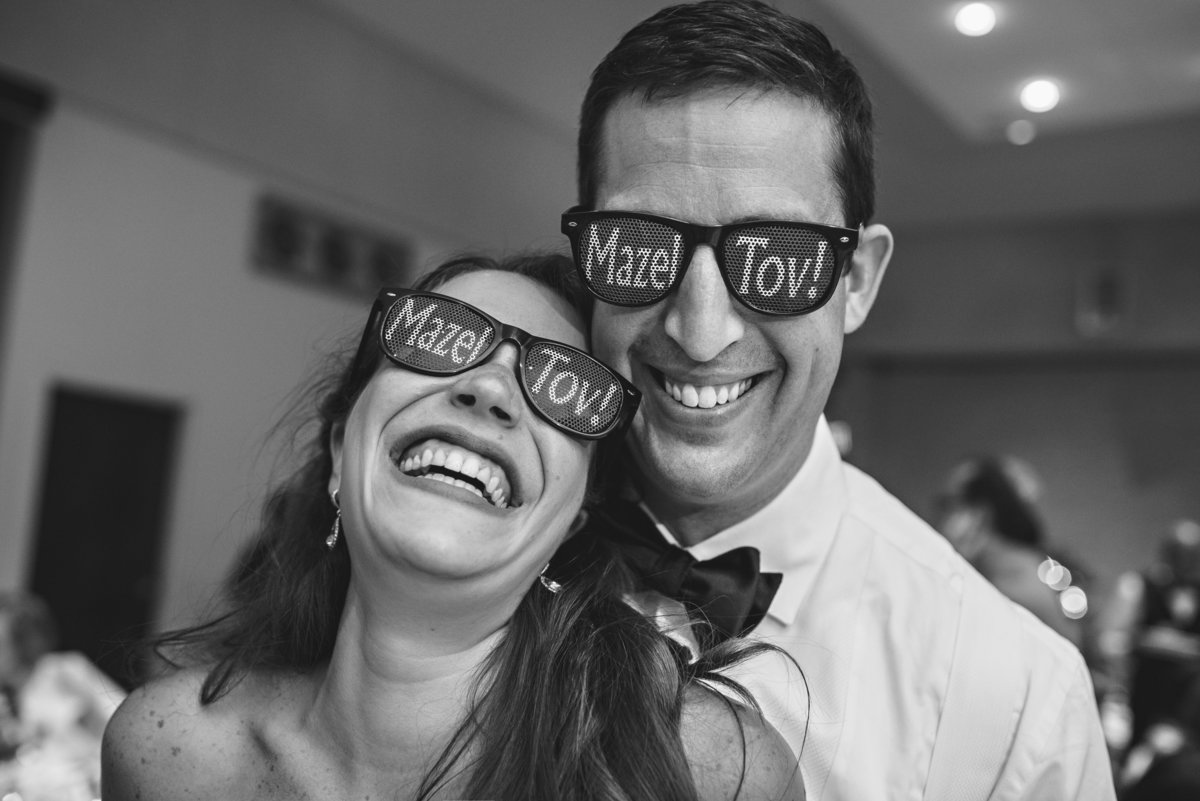 A bride and groom wearing sunglasses that say mazel tov.