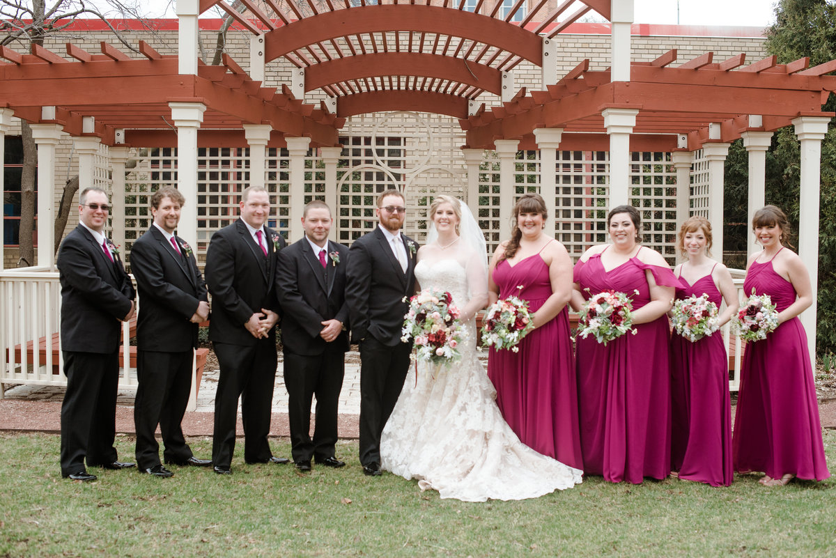 Wedding party with groomsmen on the left side by the husband and the bridesmaids on the right next to the bride
