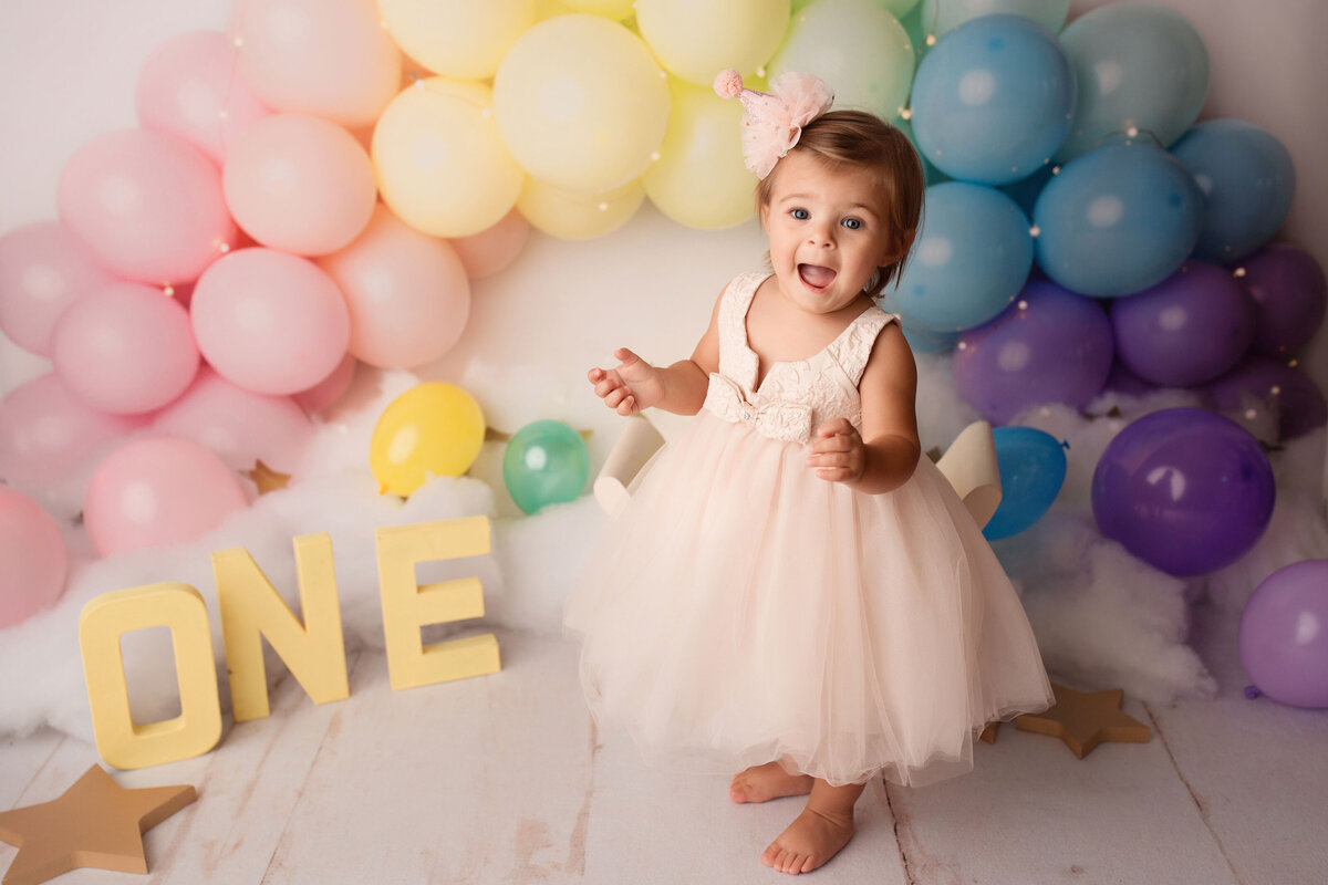 baby girl standing next to the balloon arch and ONE letters