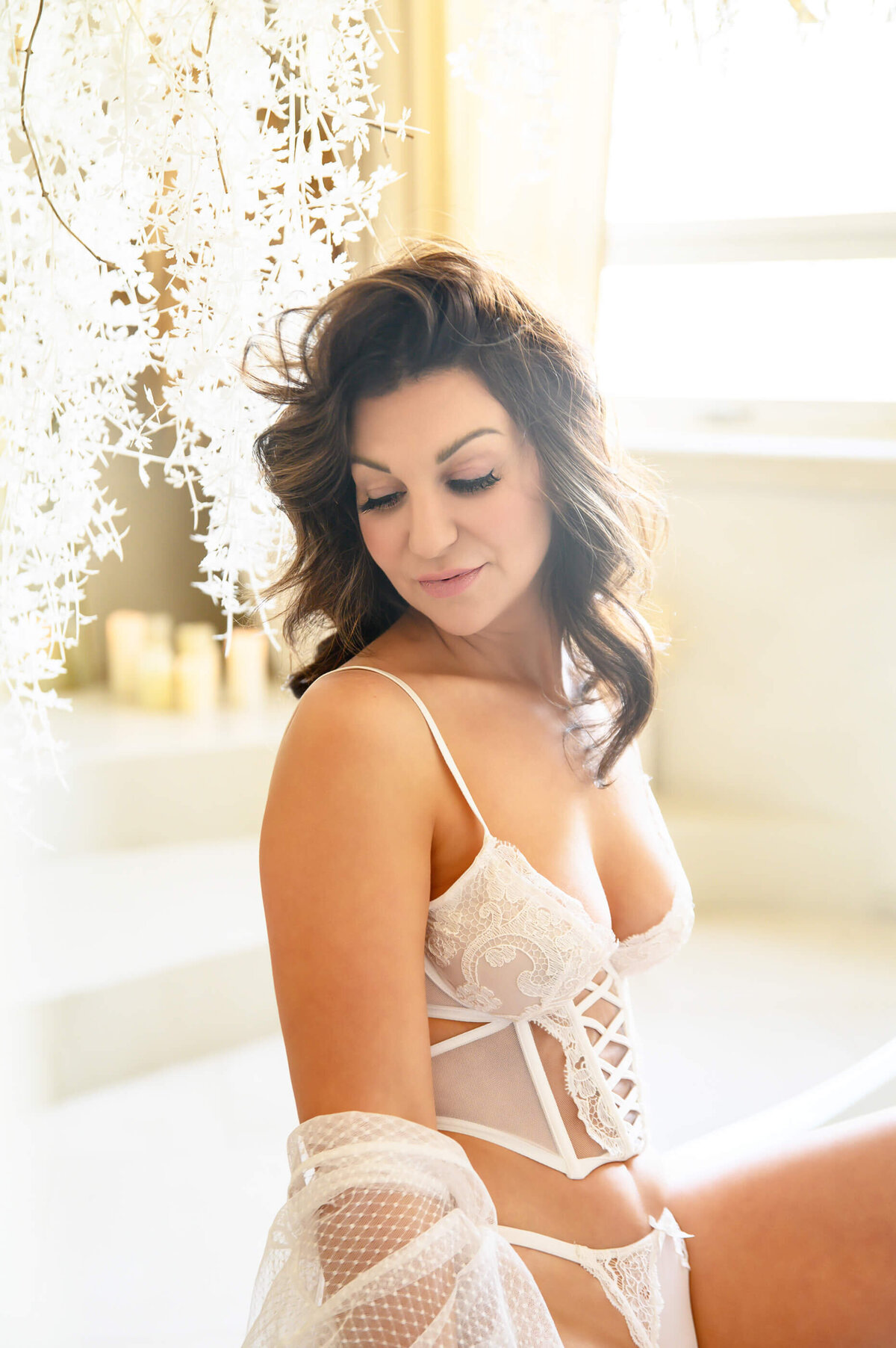 Brown haired woman wearing white lace with white pampas hanging down for her Mississauga boudoir photography session.