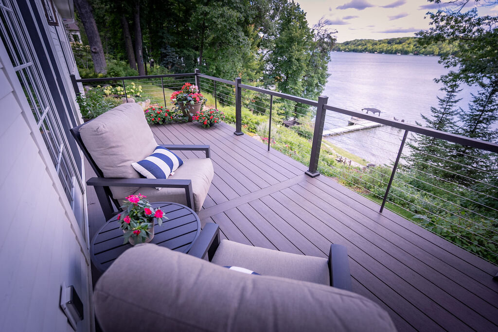 PVC deck with cable railing and outdoor seating overlooking a Minnesota lake and lush trees in summer. 