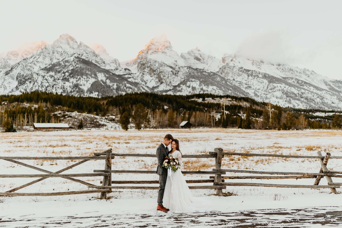 A bride and groom standing in front of a snow covered field below the Grand Teton in Grand Teton National Park