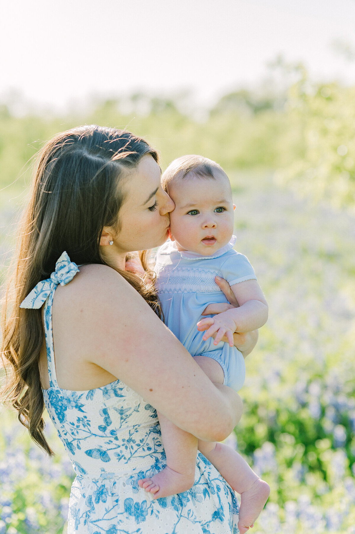 Mother kissing her baby son in a field of bluebonnets.