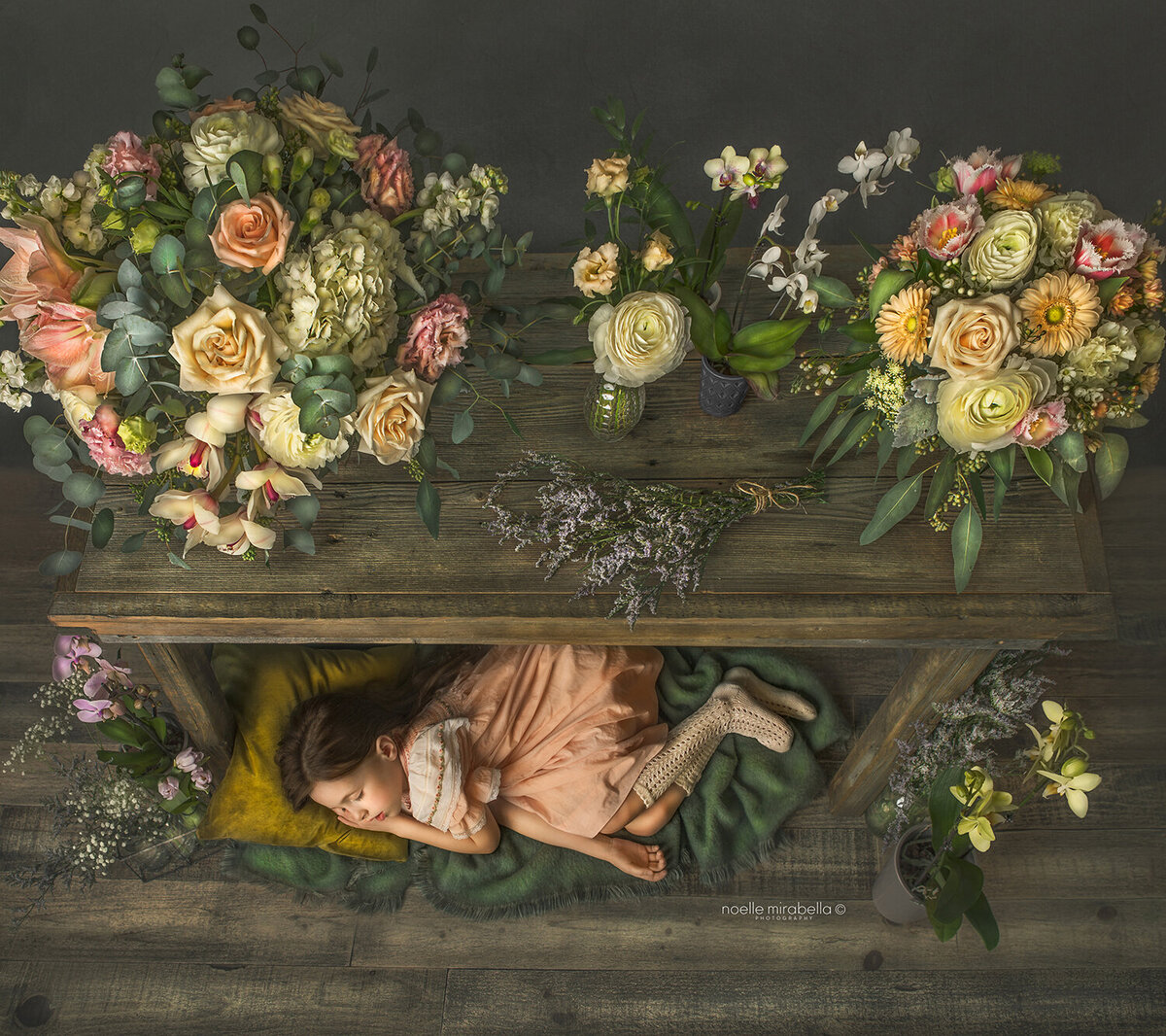Girl sleeping under table of peach , pink, and cream flowers.