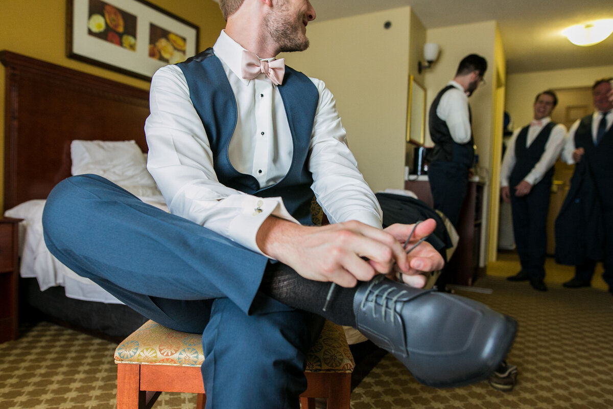 njeri-bishota-lauren-ashley-groom-square-toed-shoes-vest-bowtie-laces-hotel-suite-getting-ready