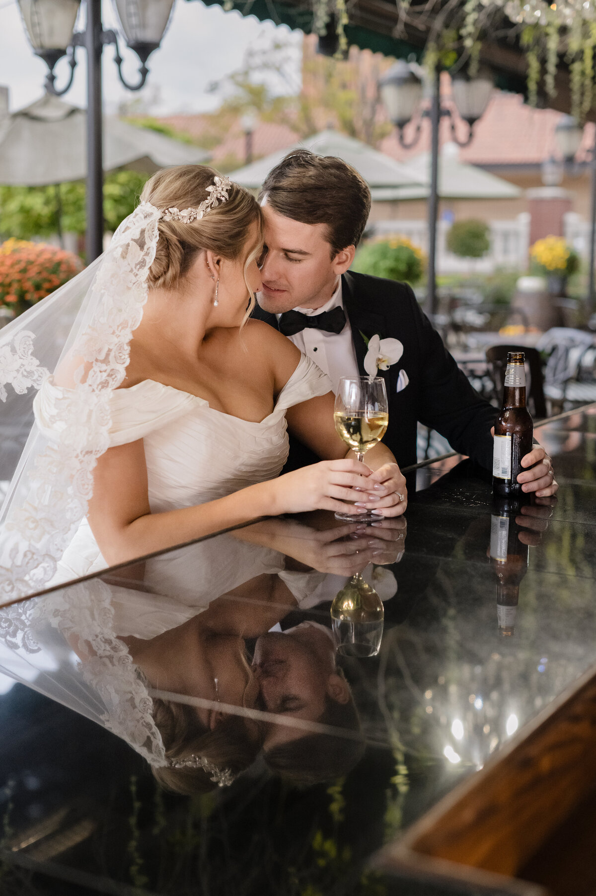 bride and groom sit at reflective tabletop bar with drinks
