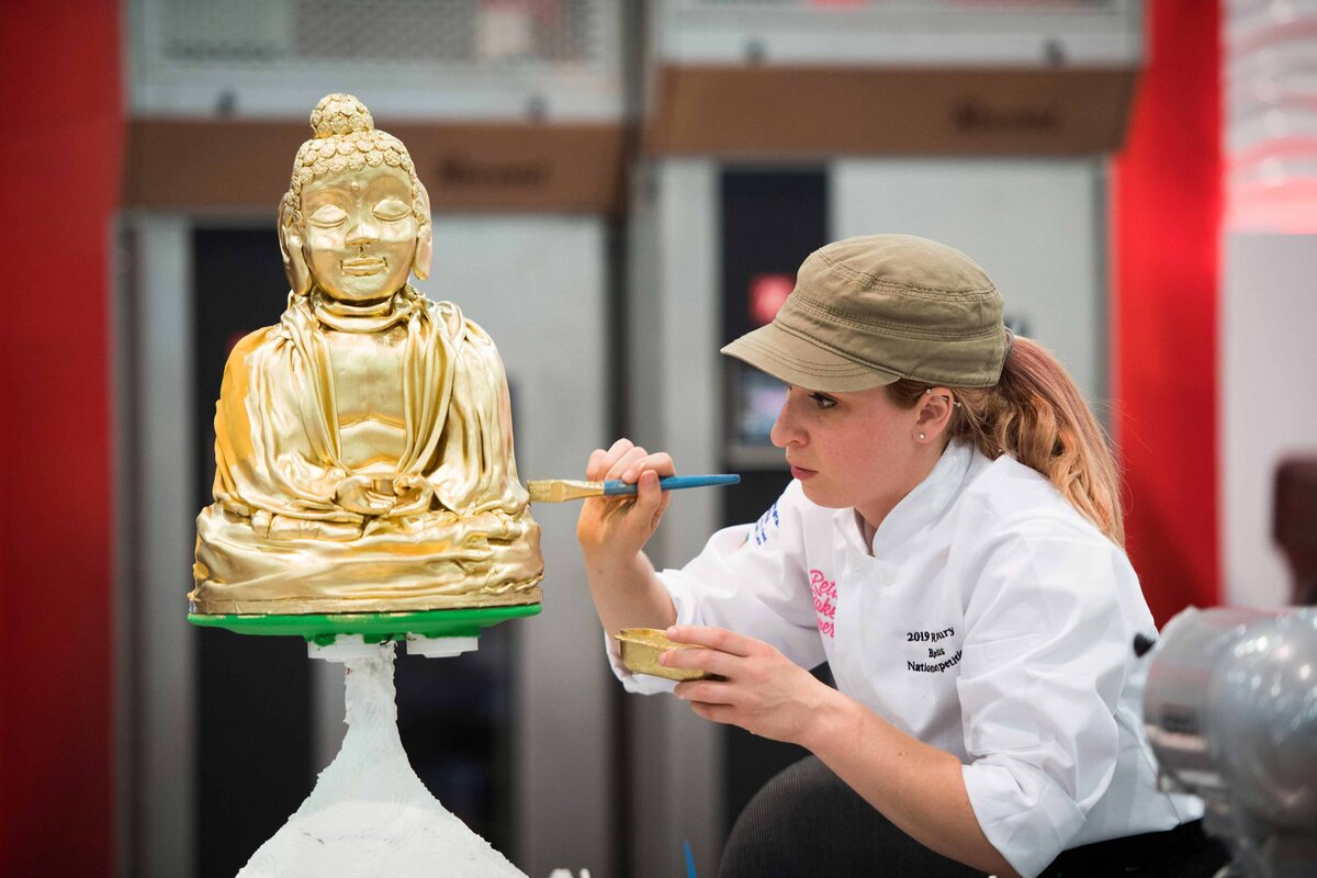 A female chef paints gold paint on a cake in the shape of a Buddha