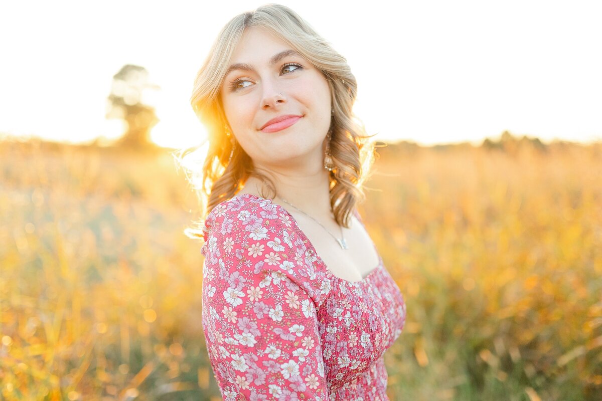 A teenage, high school senior, girl in a field at sunset in during a senior photo session in Lexington KY.