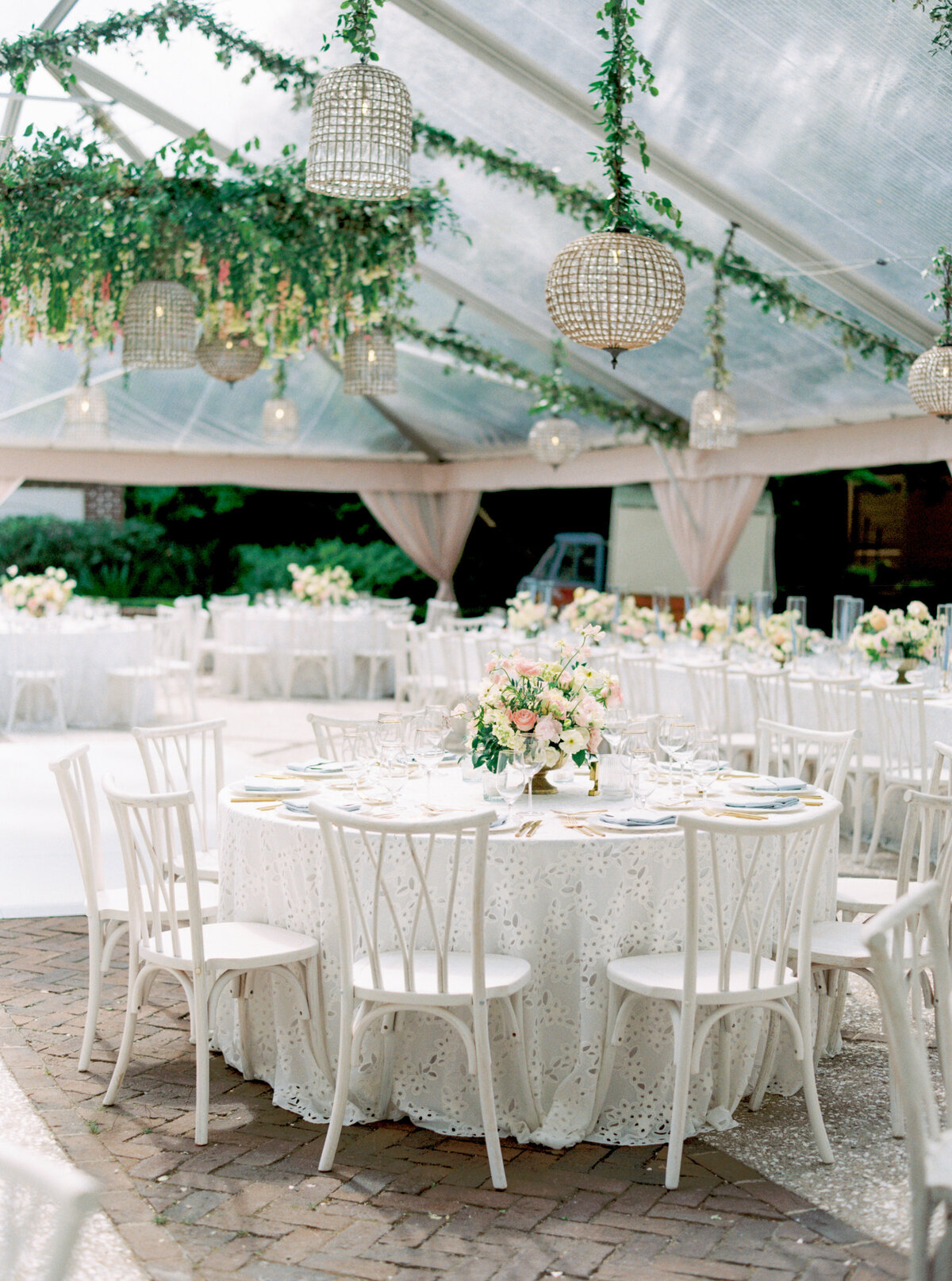 Light and bright spring wedding reception design. Bird cage lighting. Clear tent and hanging greenery with flowers.