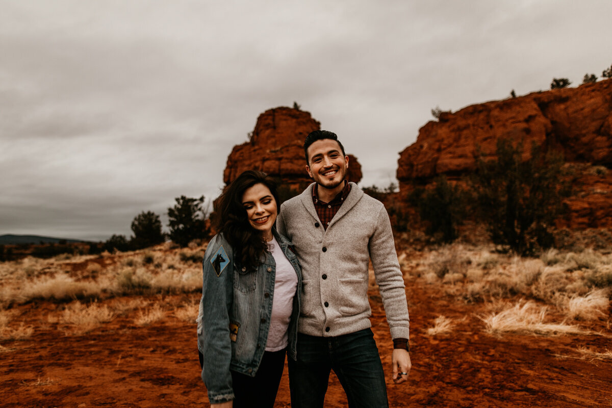 engaged couple walking in front of red rocks laughing