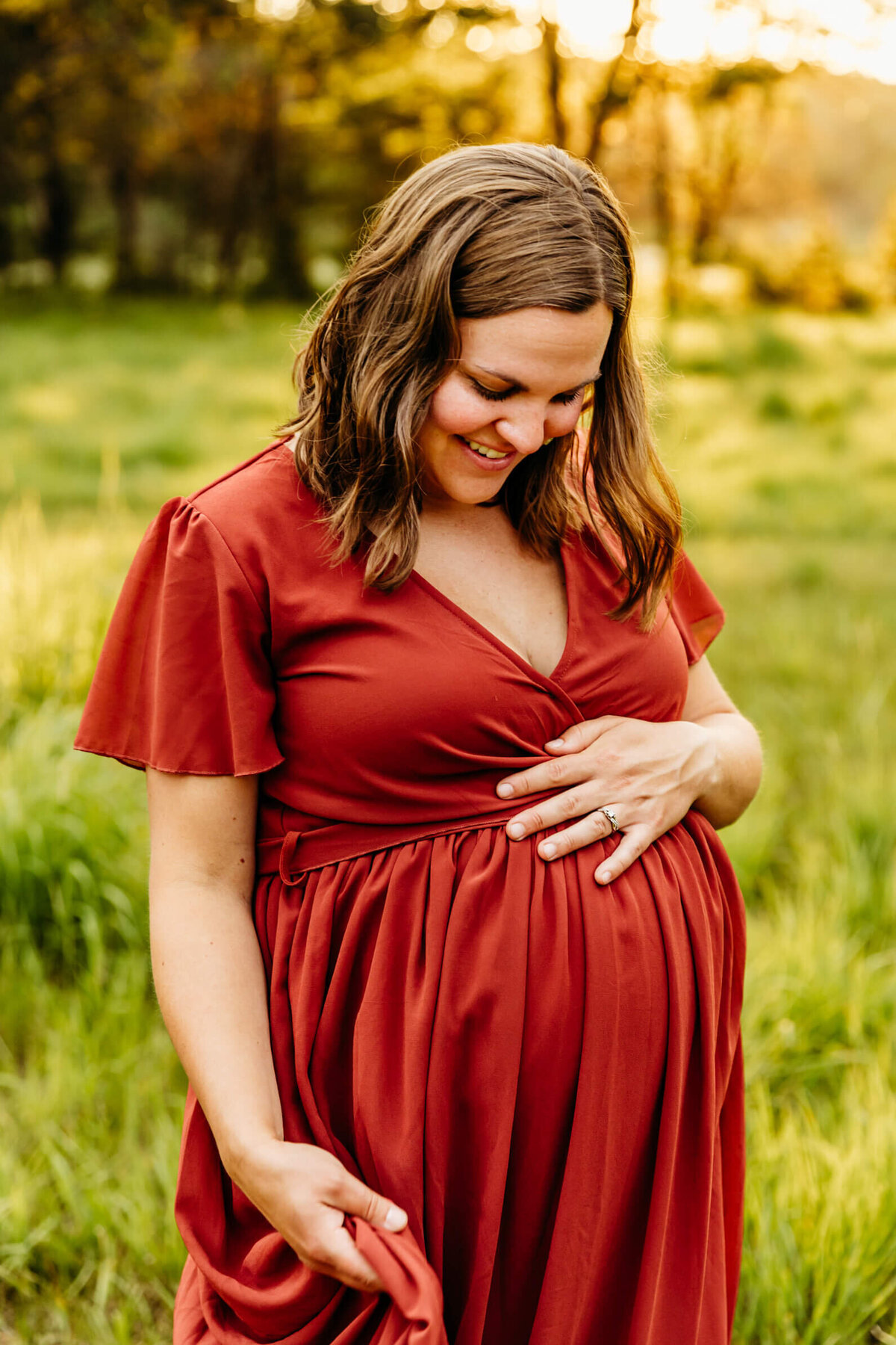 beautiful expecting mama holding bump and playing with her red dress by Ashley Kalbus